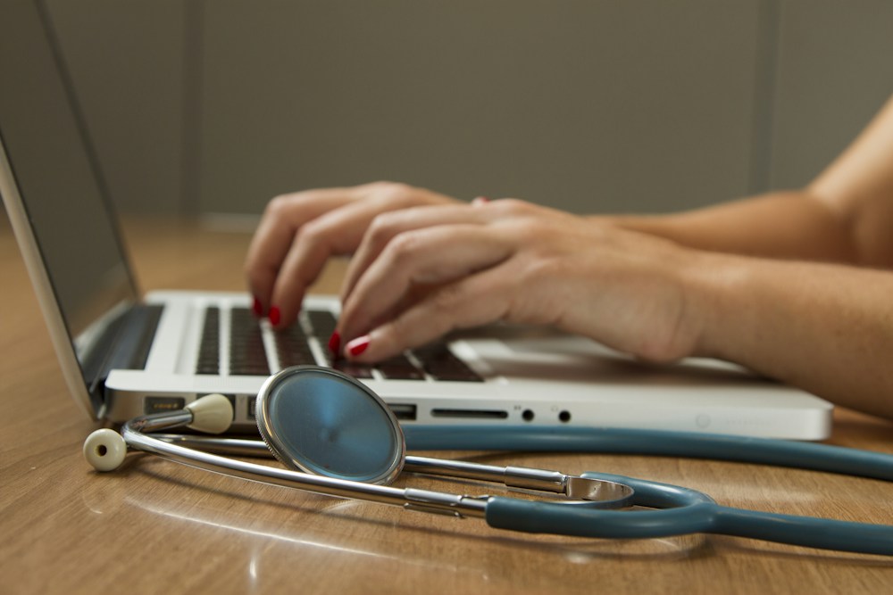 Stethoscope and a healthcare professional reviewing information on a laptop
